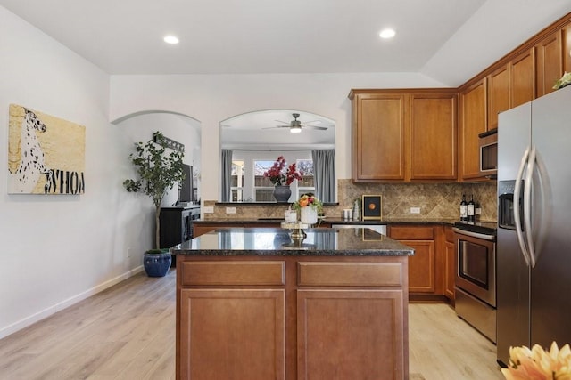 kitchen with tasteful backsplash, dark stone countertops, a center island, stainless steel appliances, and light wood-type flooring