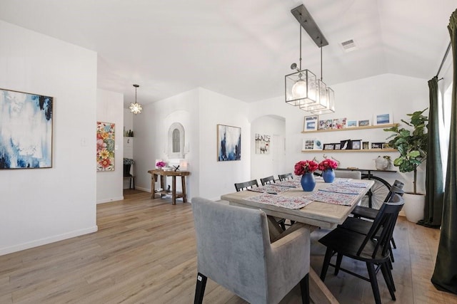 dining space featuring arched walkways, visible vents, vaulted ceiling, light wood-type flooring, and baseboards