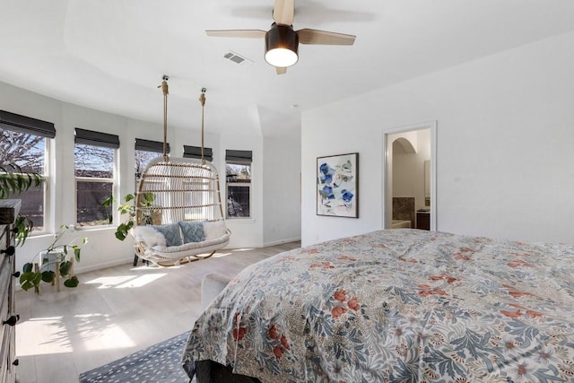 bedroom with arched walkways, visible vents, baseboards, and wood finished floors