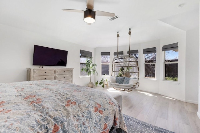 bedroom with a ceiling fan, visible vents, baseboards, and wood finished floors