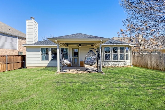 rear view of property with a ceiling fan, a fenced backyard, a yard, and a shingled roof