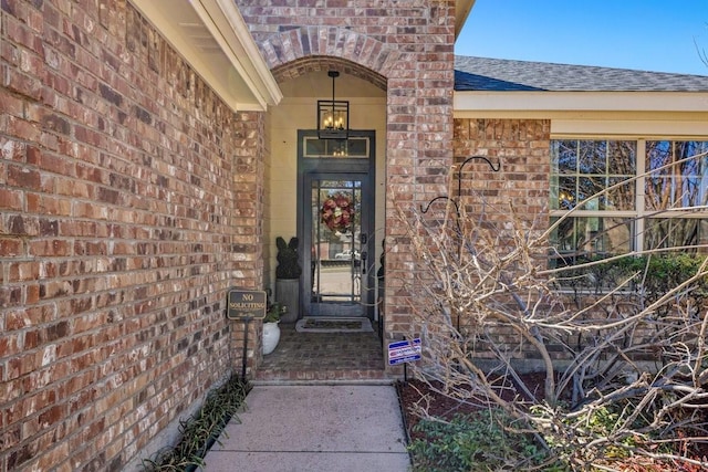 doorway to property with a shingled roof and brick siding