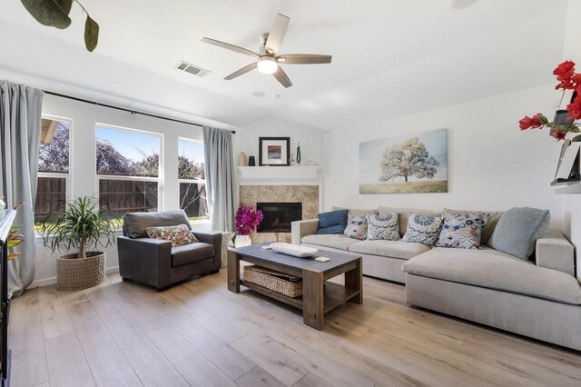 living area featuring wood finished floors, visible vents, a ceiling fan, vaulted ceiling, and a glass covered fireplace