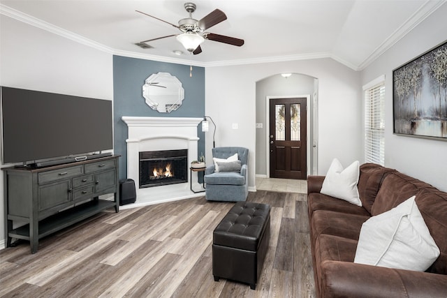 living area featuring ornamental molding, arched walkways, a lit fireplace, and wood finished floors