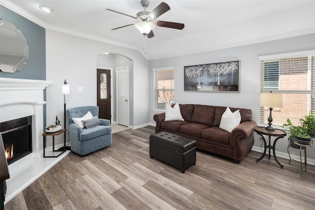 living room featuring arched walkways, baseboards, light wood-style floors, a lit fireplace, and ornamental molding