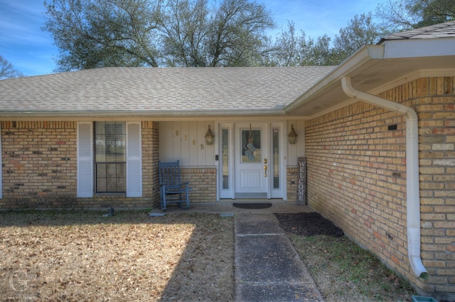 view of exterior entry featuring brick siding, a porch, and a shingled roof