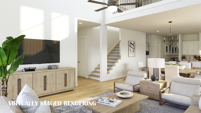 living room featuring baseboards, a towering ceiling, stairway, light wood-style floors, and ceiling fan with notable chandelier