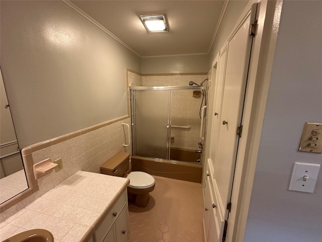 bathroom with bath / shower combo with glass door, toilet, ornamental molding, vanity, and tile walls