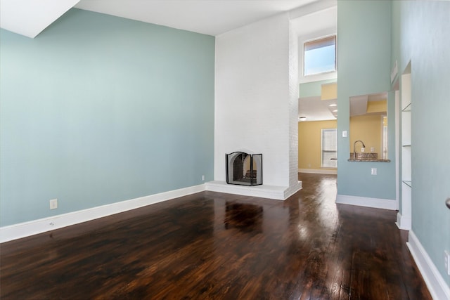 unfurnished living room featuring a brick fireplace, a towering ceiling, baseboards, and wood finished floors