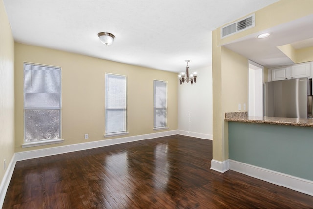 unfurnished room featuring a chandelier, dark wood-style flooring, visible vents, and baseboards