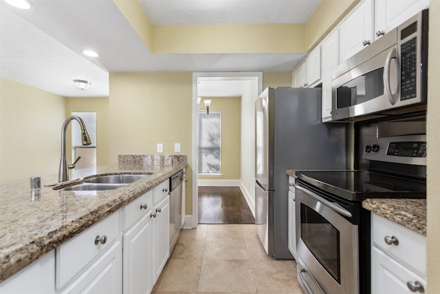 kitchen with appliances with stainless steel finishes, a sink, light stone counters, and white cabinets