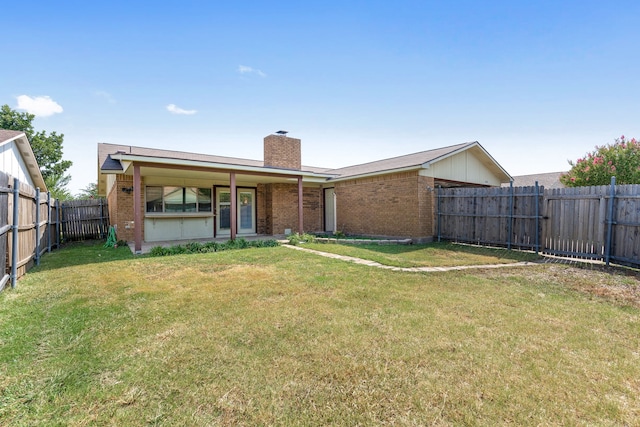 rear view of property featuring a yard, brick siding, a chimney, and a fenced backyard