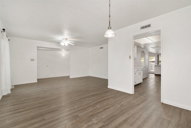 spare room featuring baseboards, ceiling fan, arched walkways, and dark wood-type flooring