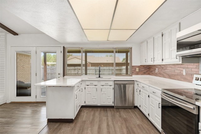 kitchen featuring stainless steel appliances, dark wood-type flooring, a peninsula, and a sink