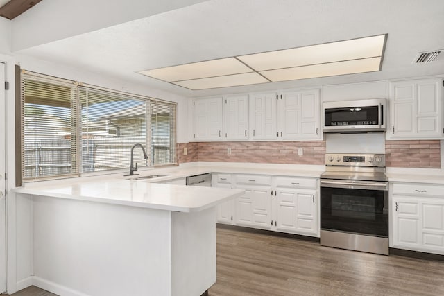 kitchen featuring visible vents, a peninsula, stainless steel appliances, white cabinetry, and a sink