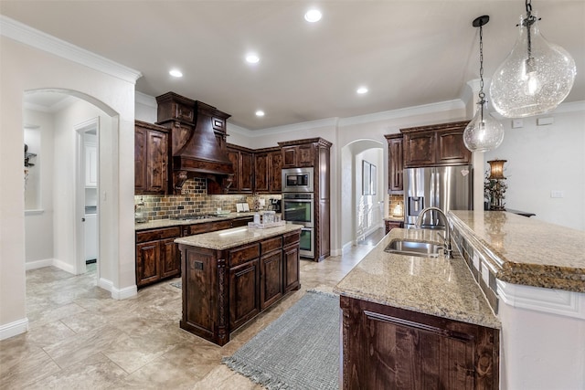 kitchen with arched walkways, stainless steel appliances, a sink, premium range hood, and a large island with sink