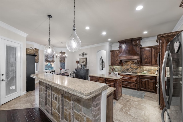 kitchen featuring tasteful backsplash, arched walkways, a center island, freestanding refrigerator, and premium range hood