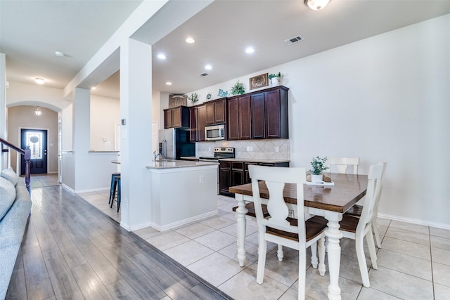 kitchen featuring dark brown cabinetry, tasteful backsplash, visible vents, arched walkways, and stainless steel appliances