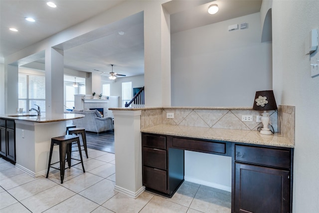 kitchen with light tile patterned floors, light stone counters, a breakfast bar, a sink, and backsplash