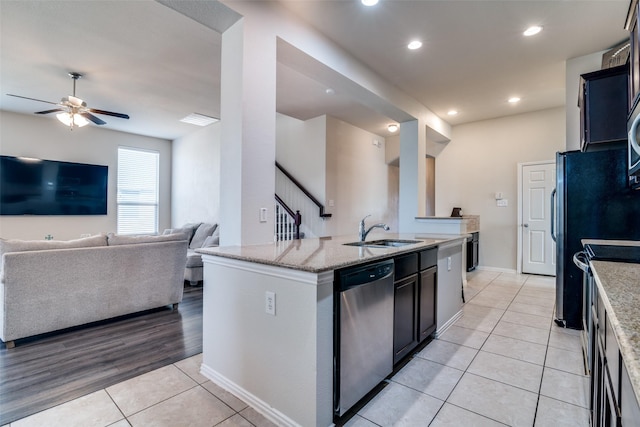 kitchen featuring light stone counters, open floor plan, stainless steel dishwasher, a sink, and light tile patterned flooring