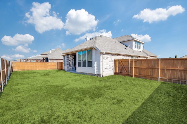 back of house featuring brick siding, a fenced backyard, roof with shingles, and a yard