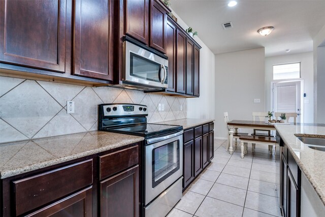 kitchen with light stone counters, stainless steel appliances, decorative backsplash, a sink, and a kitchen bar