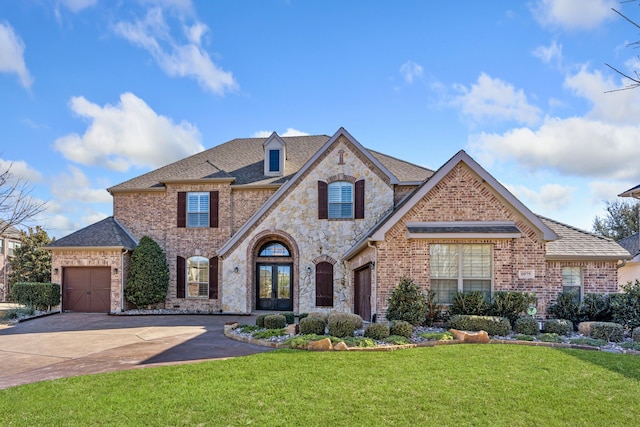 french country home featuring a garage, brick siding, driveway, stone siding, and a front lawn