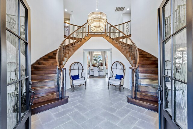 entrance foyer with stairs, a towering ceiling, visible vents, and an inviting chandelier