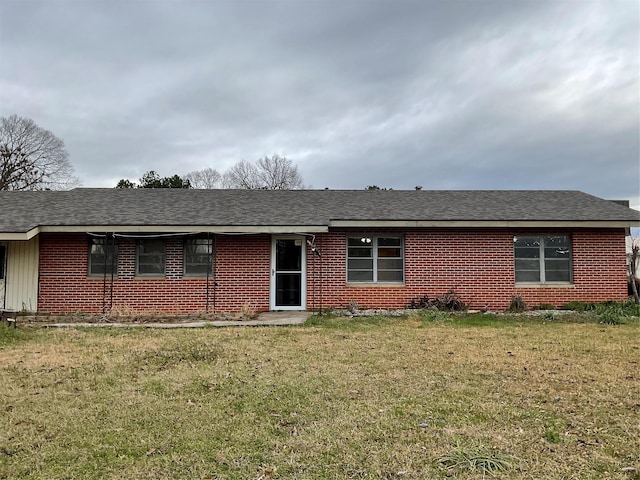 single story home with a shingled roof, a front yard, and brick siding