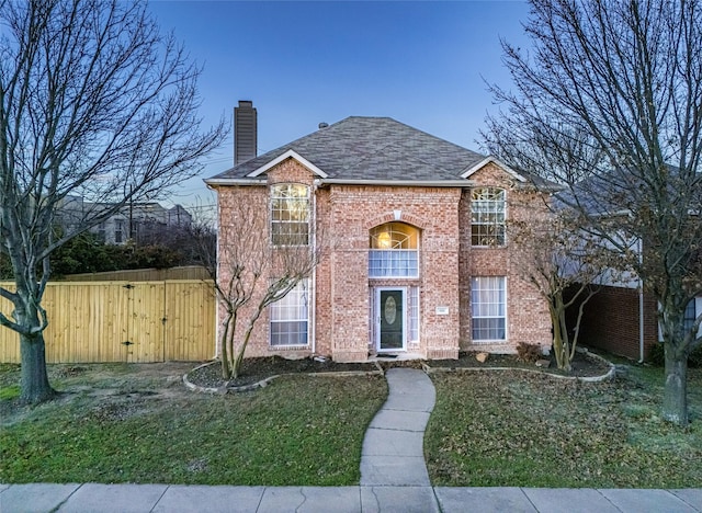 traditional home featuring a balcony, a gate, a chimney, a front lawn, and brick siding