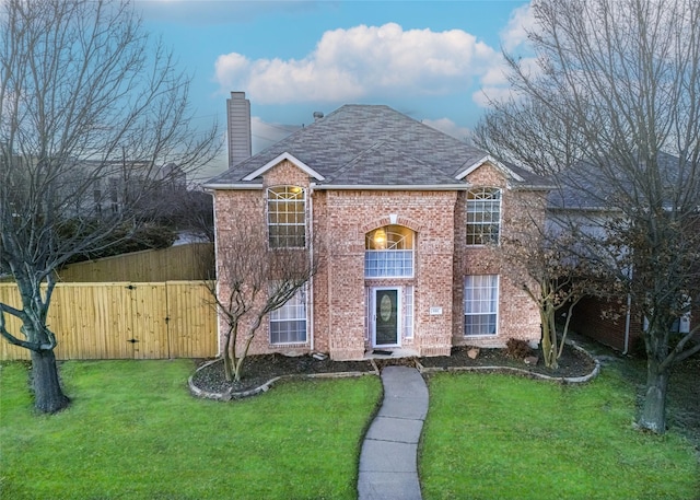 traditional home featuring a balcony, a gate, a chimney, a front lawn, and brick siding