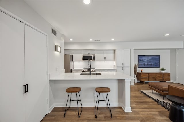 kitchen featuring white cabinets, a kitchen breakfast bar, wood finished floors, stainless steel appliances, and recessed lighting