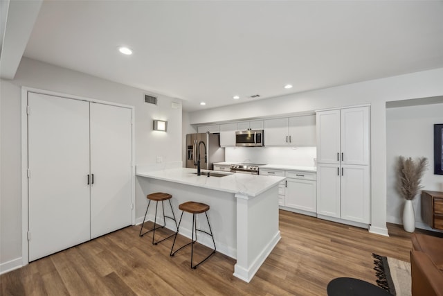 kitchen featuring a peninsula, wood finished floors, white cabinetry, a kitchen breakfast bar, and appliances with stainless steel finishes