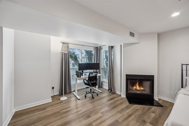 home office with recessed lighting, wood finished floors, visible vents, baseboards, and a lit fireplace