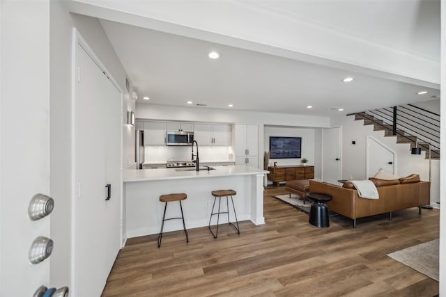 kitchen featuring appliances with stainless steel finishes, wood finished floors, a peninsula, light countertops, and a kitchen bar