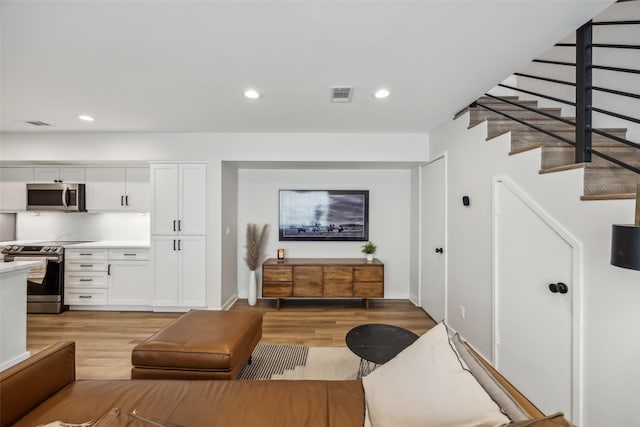 living room with recessed lighting, visible vents, baseboards, light wood-style floors, and stairway