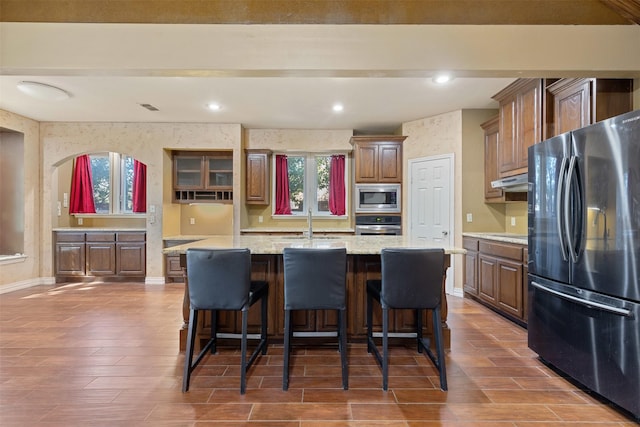 kitchen with baseboards, beamed ceiling, a kitchen island with sink, stainless steel appliances, and a sink