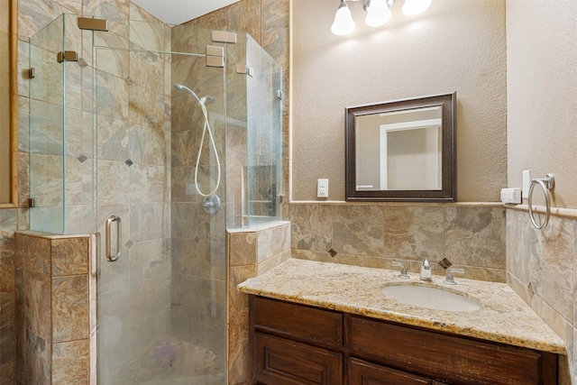 bathroom featuring a wainscoted wall, a stall shower, vanity, and tile walls