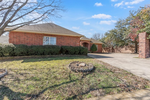 ranch-style house with a shingled roof, brick siding, driveway, and a front lawn