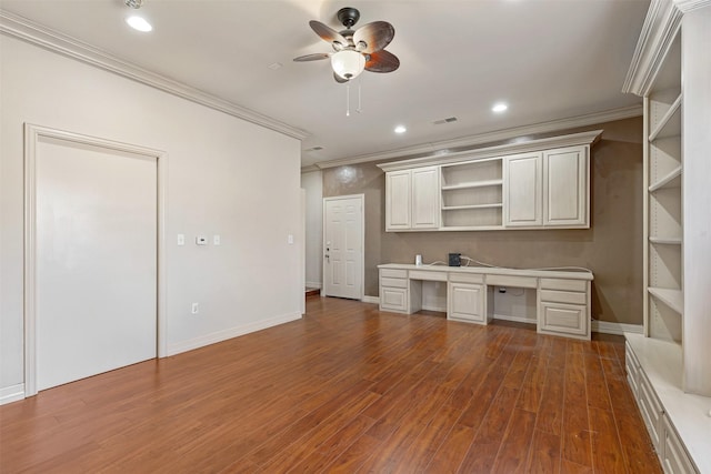 unfurnished office with built in desk, dark wood-style flooring, visible vents, and crown molding