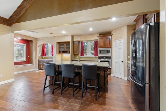 kitchen with wallpapered walls, a center island with sink, baseboards, appliances with stainless steel finishes, and a kitchen bar