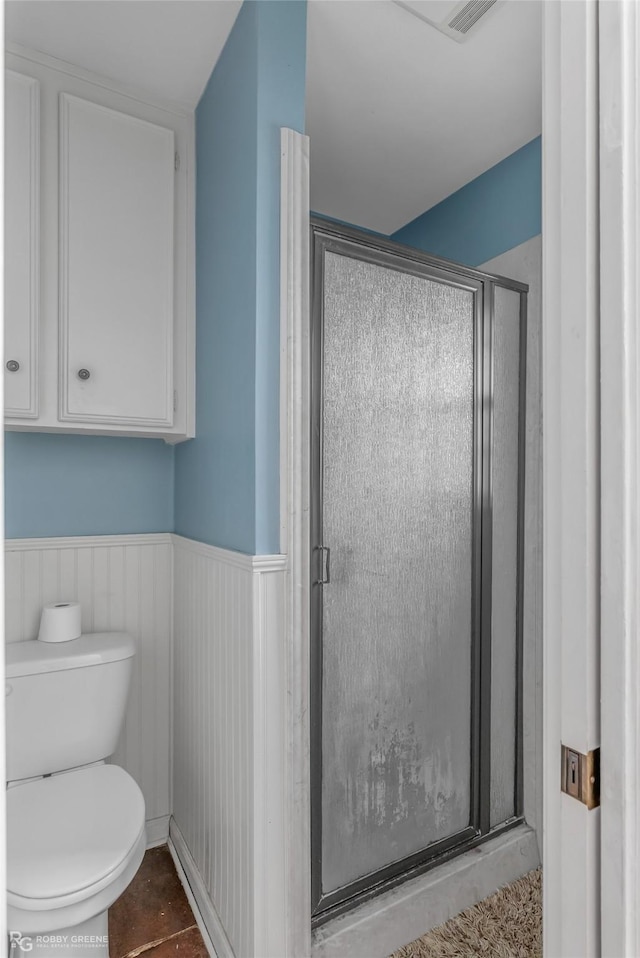 bathroom with a stall shower, a wainscoted wall, and toilet