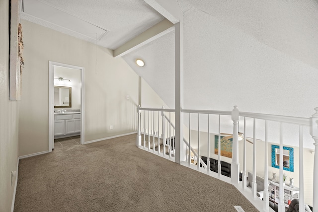 corridor with a textured ceiling, vaulted ceiling with beams, baseboards, carpet, and attic access