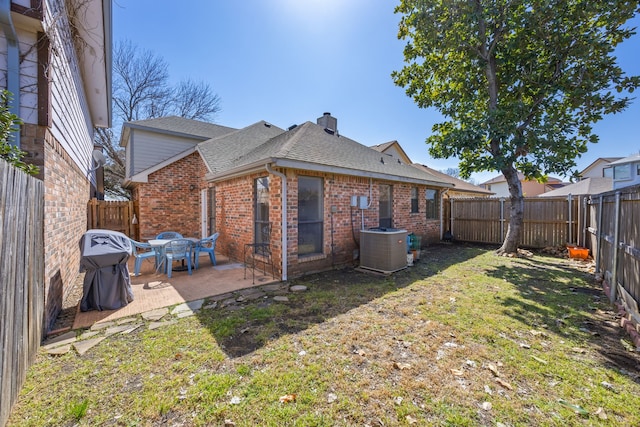 rear view of house with brick siding, a patio, a chimney, a lawn, and a fenced backyard