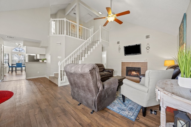 living area with visible vents, a tiled fireplace, wood finished floors, baseboards, and stairs