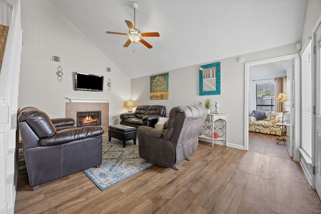 living area with a ceiling fan, a tile fireplace, visible vents, and wood finished floors