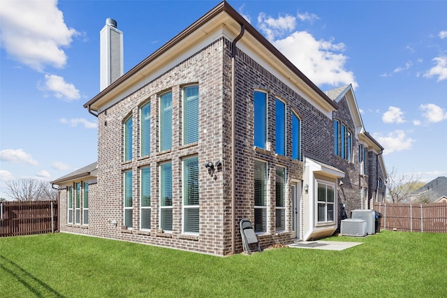 rear view of house featuring a chimney, fence, a lawn, and brick siding