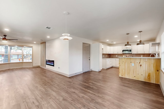 unfurnished living room featuring ceiling fan, recessed lighting, wood finished floors, visible vents, and a glass covered fireplace