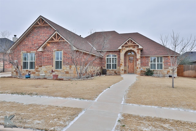 craftsman inspired home with stone siding, brick siding, a shingled roof, and fence