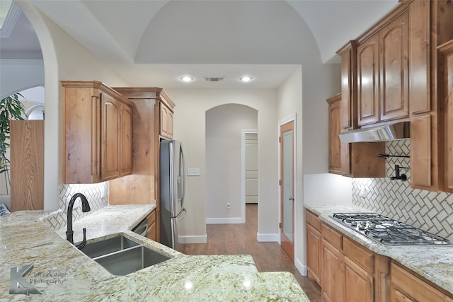 kitchen featuring appliances with stainless steel finishes, vaulted ceiling, a sink, light stone countertops, and under cabinet range hood